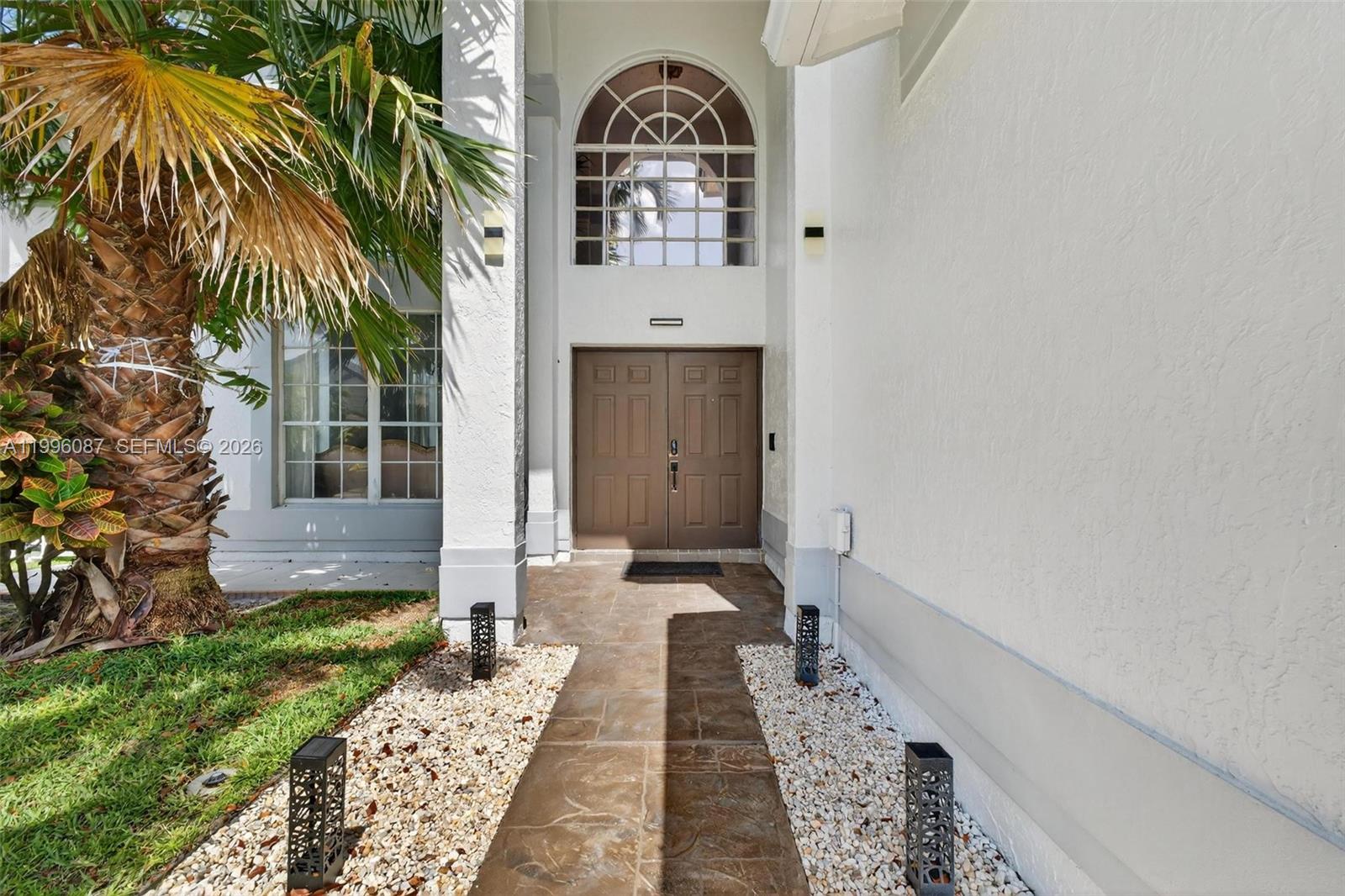 A stone walkway leads to a double-door entrance beneath an arched window — 18498 E Covington Trce, Boca Raton FL 33498, BOCA RATON, FL
