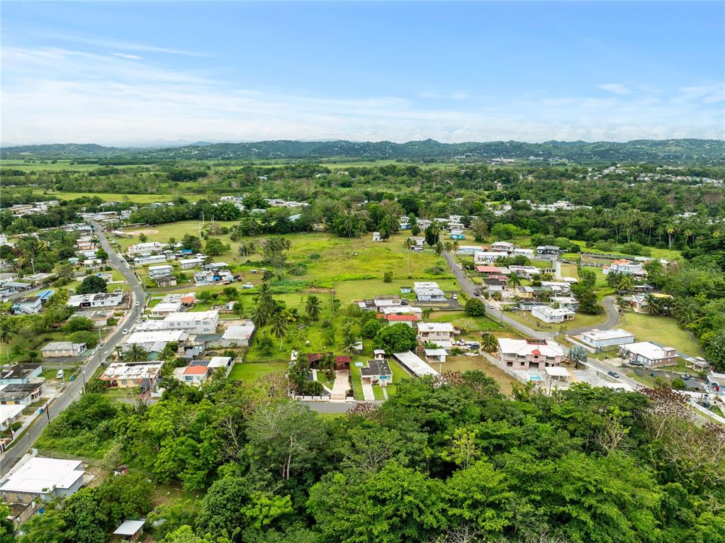 An aerial view shows a residential neighborhood surrounded by lush green trees and distant mountains — PR-442 CORNER MUNICIPAL STREET, AGUADA, PR