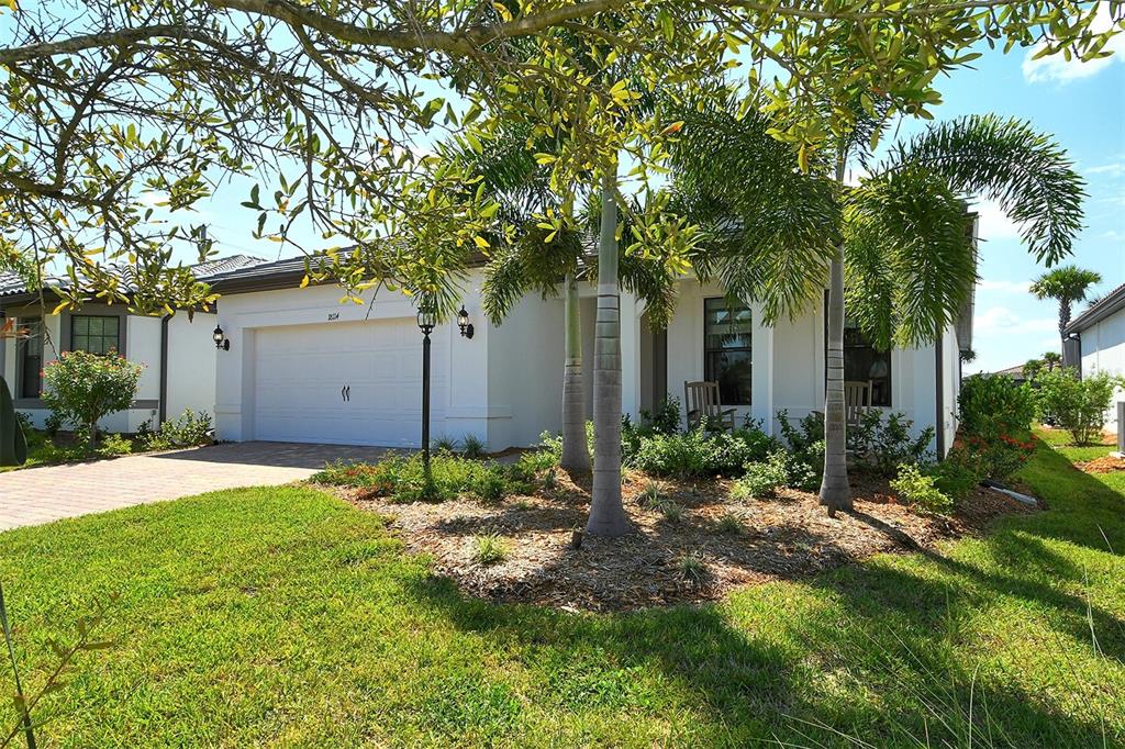 A white single-story house with a two-car garage, palm trees, and a landscaped front yard — 18114 WATERVILLE PLACE, BRADENTON, FL