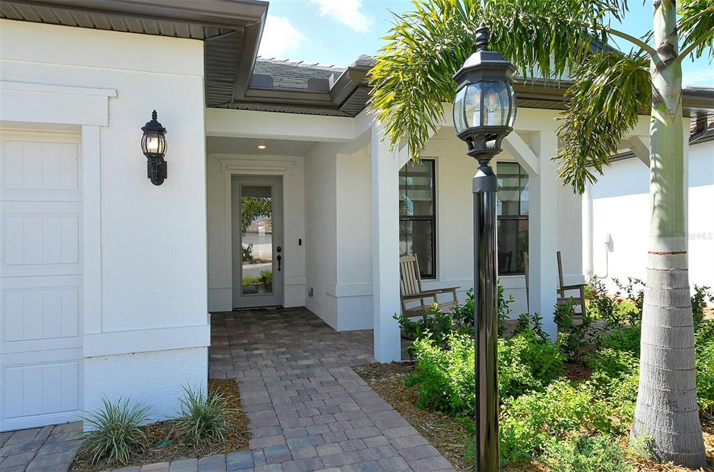 A paved walkway leads to the front entrance of a white house with a palm tree — 18114 WATERVILLE PLACE, BRADENTON, FL