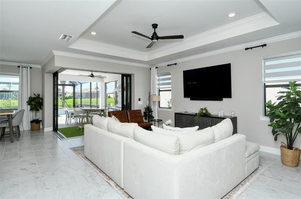 A living room features a white sectional sofa, a large television, and sliding glass doors — 18114 WATERVILLE PLACE, BRADENTON, FL