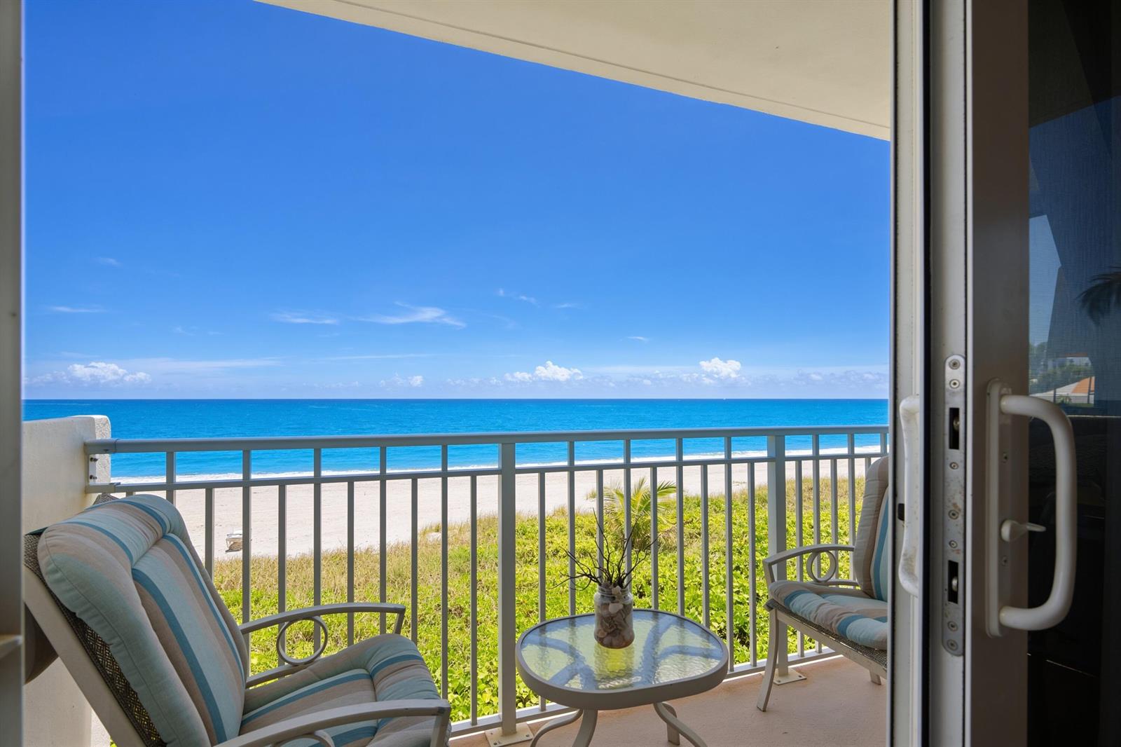 A balcony with two chairs and a small table overlooks a beach and the ocean — 3301 S Ocean Boulevard # 109, Highland Beach FL 33487, HIGHLAND BEACH, FL