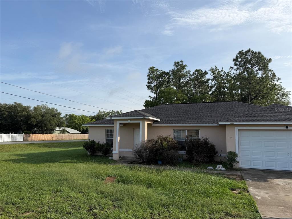 A single-story house with a tan exterior, a dark shingled roof, and a white garage door — 19 PECAN PASS TERRACE, OCALA, FL
