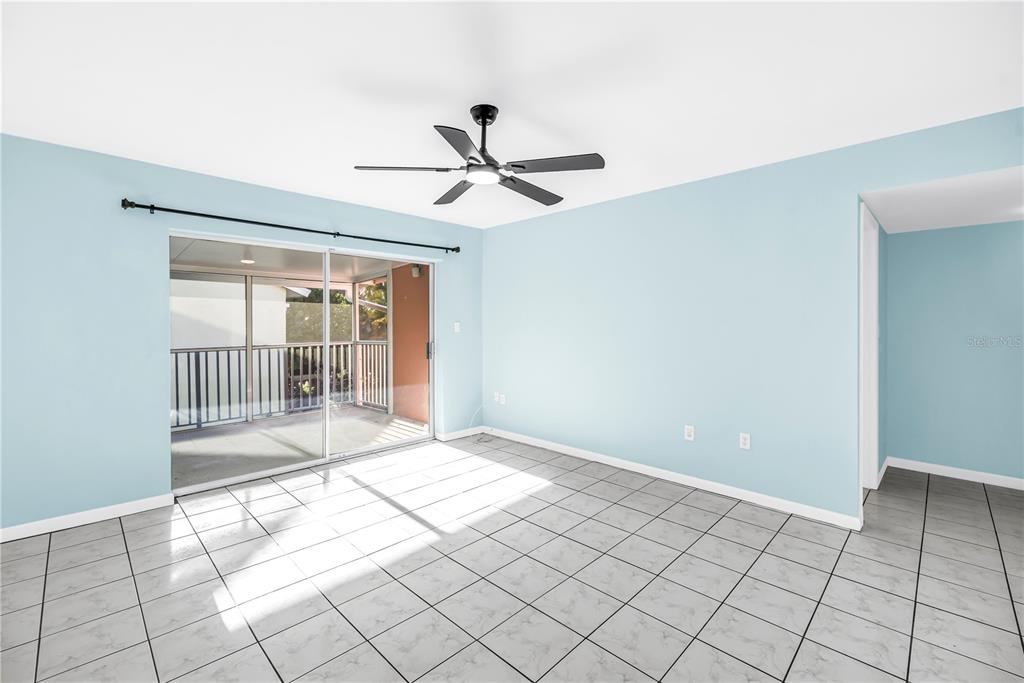 An empty room with light blue walls, tile flooring, a ceiling fan, and sliding glass doors — 3795 41ST LANE S UNIT H, ST PETERSBURG, FL
