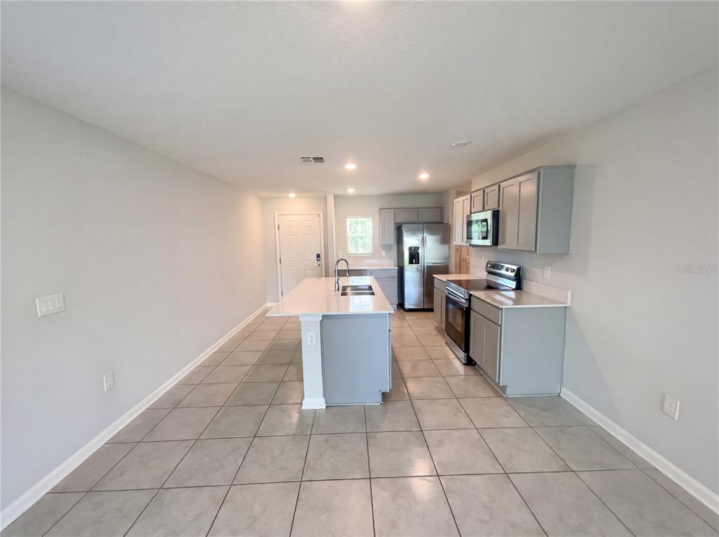 A kitchen features gray cabinets, stainless steel appliances, a center island, and tiled flooring — 4322 SUNNY CREEK PLACE, KISSIMMEE, FL