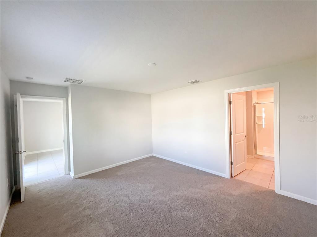 An empty bedroom with beige carpet, light gray walls, and two open doorways — 4322 SUNNY CREEK PLACE, KISSIMMEE, FL
