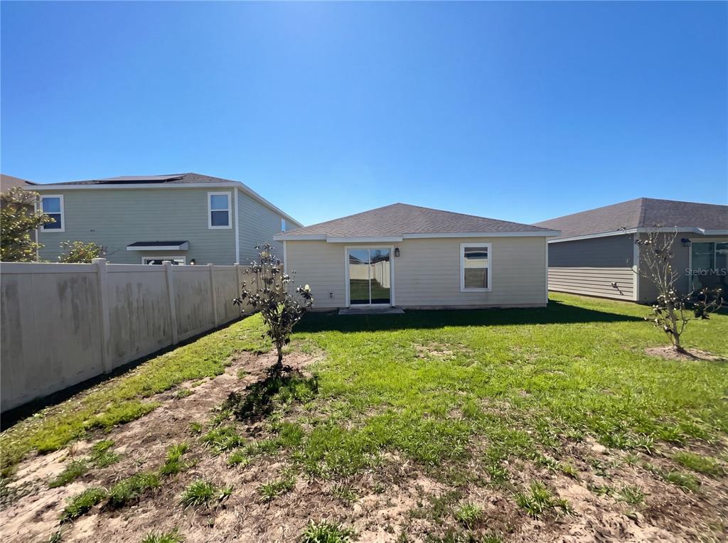 The exterior rear view of a single-story house features a sliding glass door and yard — 4322 SUNNY CREEK PLACE, KISSIMMEE, FL