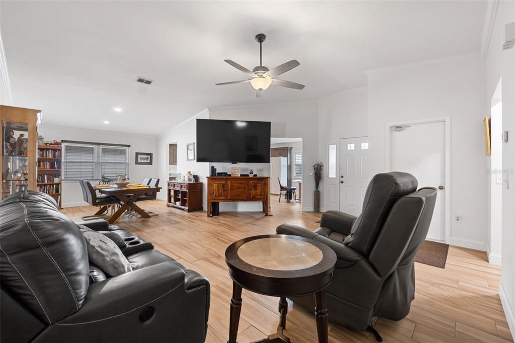 A living room with wood-look tile flooring, a ceiling fan, and a large wall-mounted television — 1957 PRAIRIE DUNES CIRCLE N, LAKELAND, FL