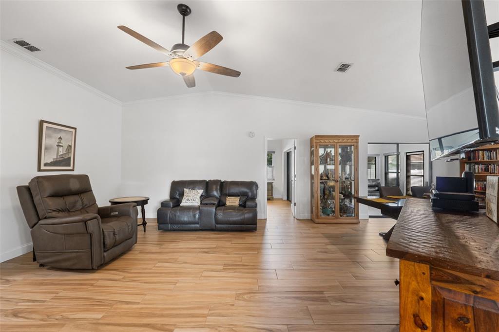 A living room features a vaulted ceiling, wood-look tile flooring, leather furniture, and a ceiling fan — 1957 PRAIRIE DUNES CIRCLE N, LAKELAND, FL