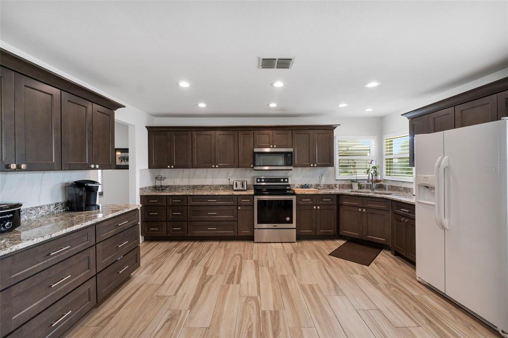 A kitchen features dark wood cabinets, granite countertops, stainless steel appliances, and light wood-look flooring — 1957 PRAIRIE DUNES CIRCLE N, LAKELAND, FL