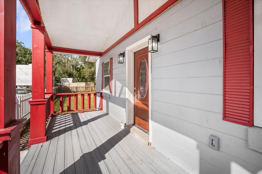 A covered porch features gray decking, red railings, and a wooden front door with glass — 15229 MYRTLE STREET, DADE CITY, FL