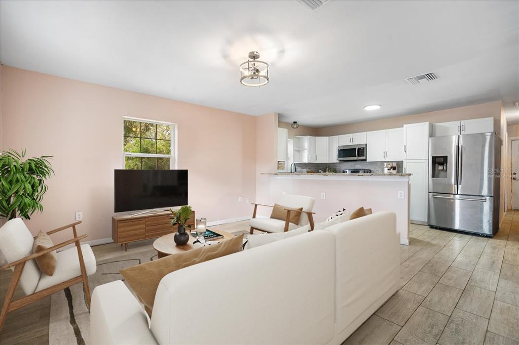A living room with light pink walls and a kitchen with white cabinets and appliances — 15229 MYRTLE STREET, DADE CITY, FL