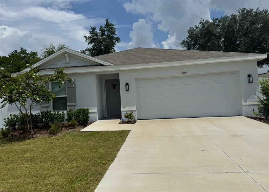 A single-story house with a white stucco exterior, a gray front door, and a concrete driveway — 3561 SW 150TH LOOP, OCALA, FL