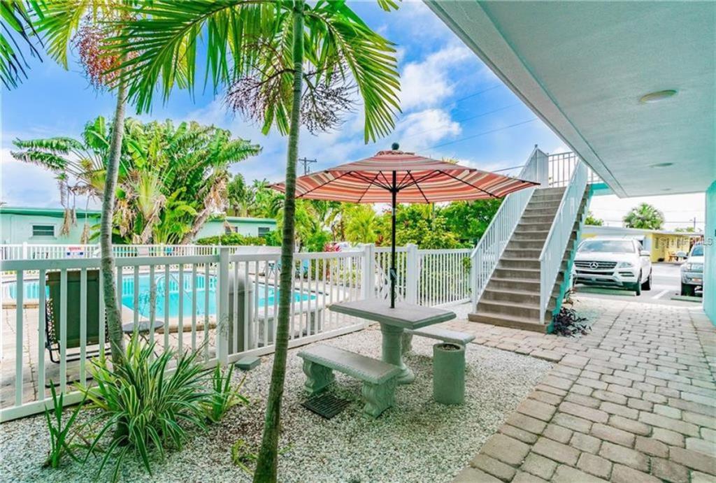 A patio area features a stone table with benches, a striped umbrella, and a swimming pool — 11440 1ST STREET E UNIT 1, TREASURE ISLAND, FL