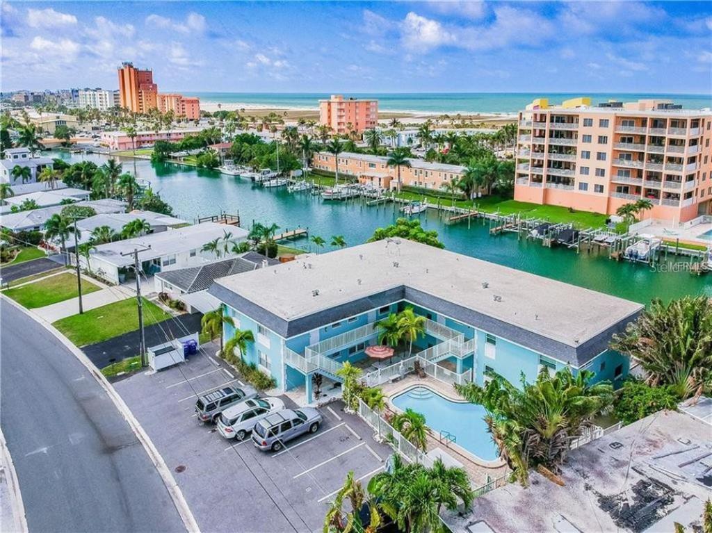 An aerial view of a blue apartment building with a pool, parking lot, and canal — 11440 1ST STREET E UNIT 1, TREASURE ISLAND, FL