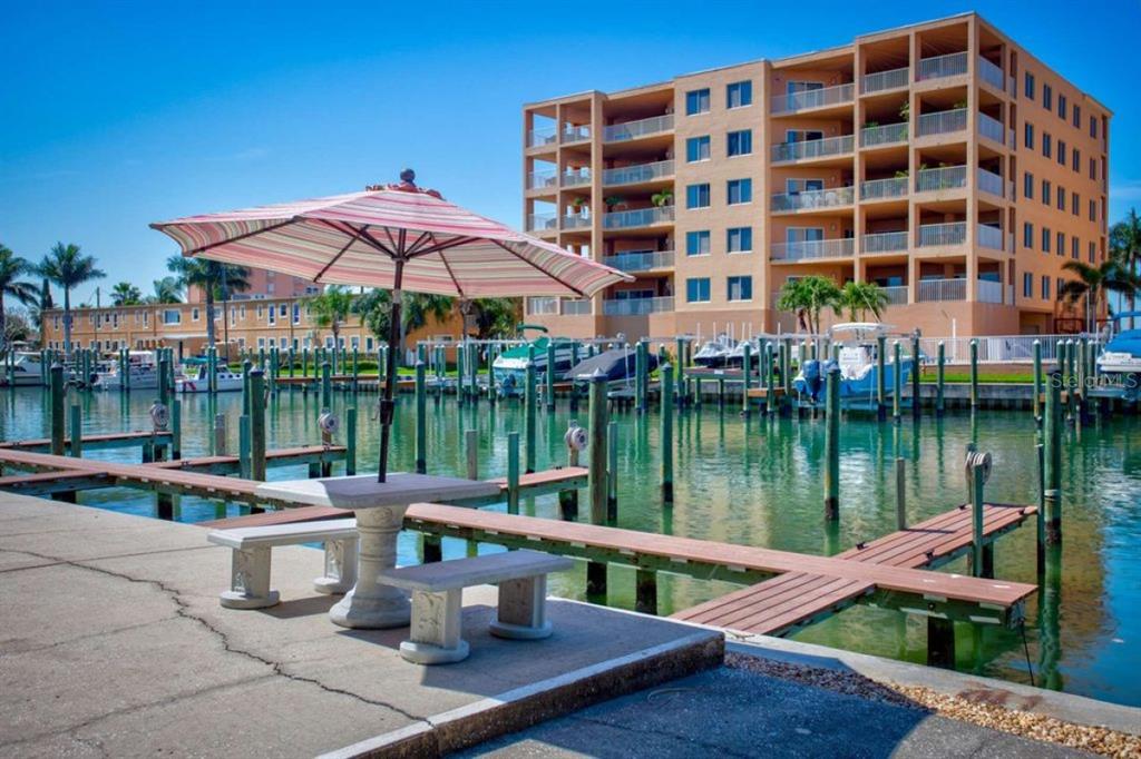 A patio table with an umbrella sits on a concrete dock overlooking a boat marina — 11440 1ST STREET E UNIT 1, TREASURE ISLAND, FL