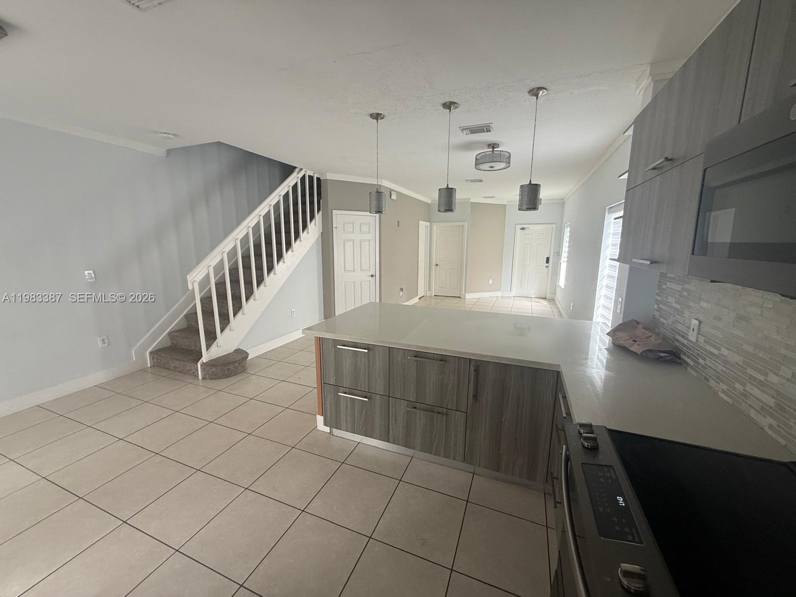 A kitchen with gray cabinets and a quartz island overlooks a living area with stairs — 10776 NW 83rd Ter # 19, Doral FL 33178, DORAL, FL
