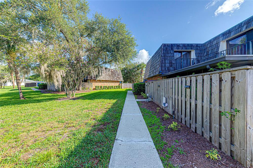 A concrete walkway runs alongside a wooden fence and a multi-story building with a balcony — 921 ROYAL OAK BOULEVARD, LEESBURG, FL