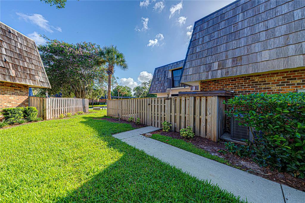 A grassy yard with a concrete walkway leads to a wooden fence and brick building — 921 ROYAL OAK BOULEVARD, LEESBURG, FL