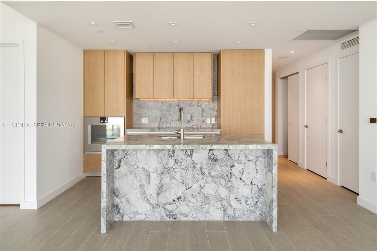 A modern kitchen features light wood cabinetry, a marble waterfall island, and marble backsplash — 500 Alton Rd # 2207, Miami Beach FL 33139, MIAMI BEACH, FL
