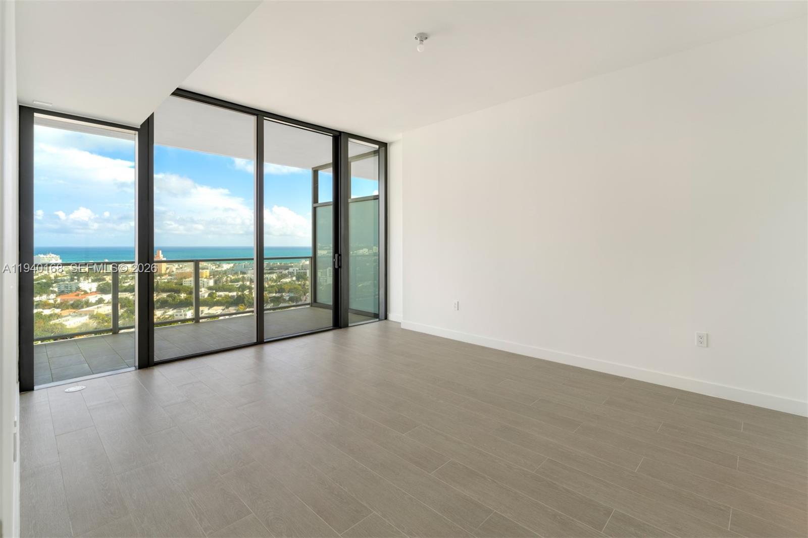 An empty room features light wood-look tile flooring, white walls, and floor-to-ceiling glass balcony doors — 500 Alton Rd # 2207, Miami Beach FL 33139, MIAMI BEACH, FL