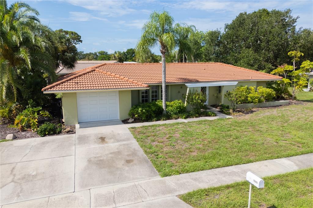 A single-story house with a terracotta tile roof, a white garage door, and palm trees — 7411 DICKENS DRIVE, SARASOTA, FL