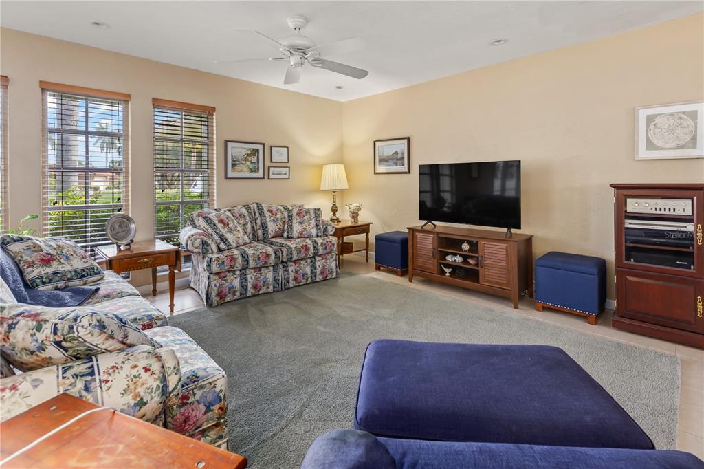 A living room features floral sofas, a television on a wooden stand, and blue ottomans — 7411 DICKENS DRIVE, SARASOTA, FL
