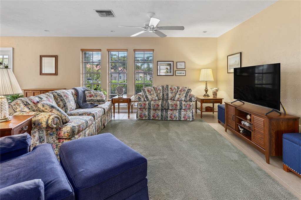 A living room features floral sofas, a blue ottoman, and a television on a wooden stand — 7411 DICKENS DRIVE, SARASOTA, FL