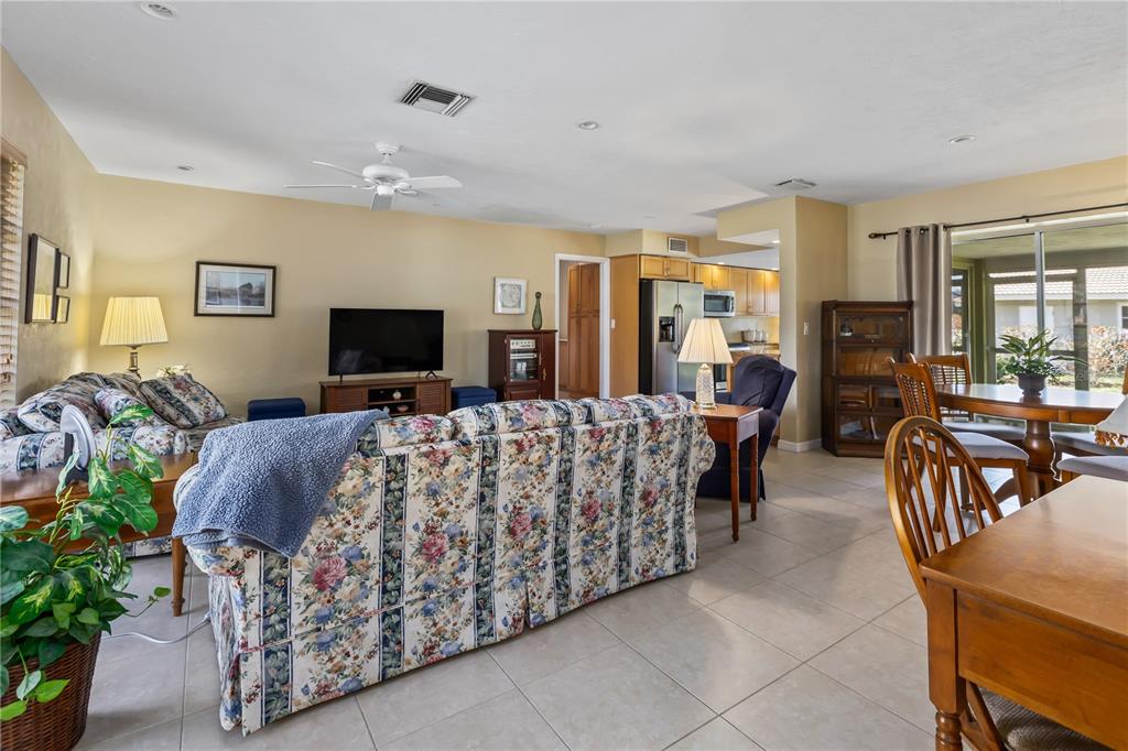 An open-concept living and dining area features floral sofas, tile flooring, and a kitchen — 7411 DICKENS DRIVE, SARASOTA, FL