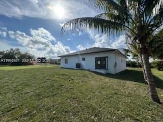 A white single-story house sits on a grassy lot under a bright, cloudy sky — 1468 NW 100th St, Miami FL 33147, MIAMI, FL