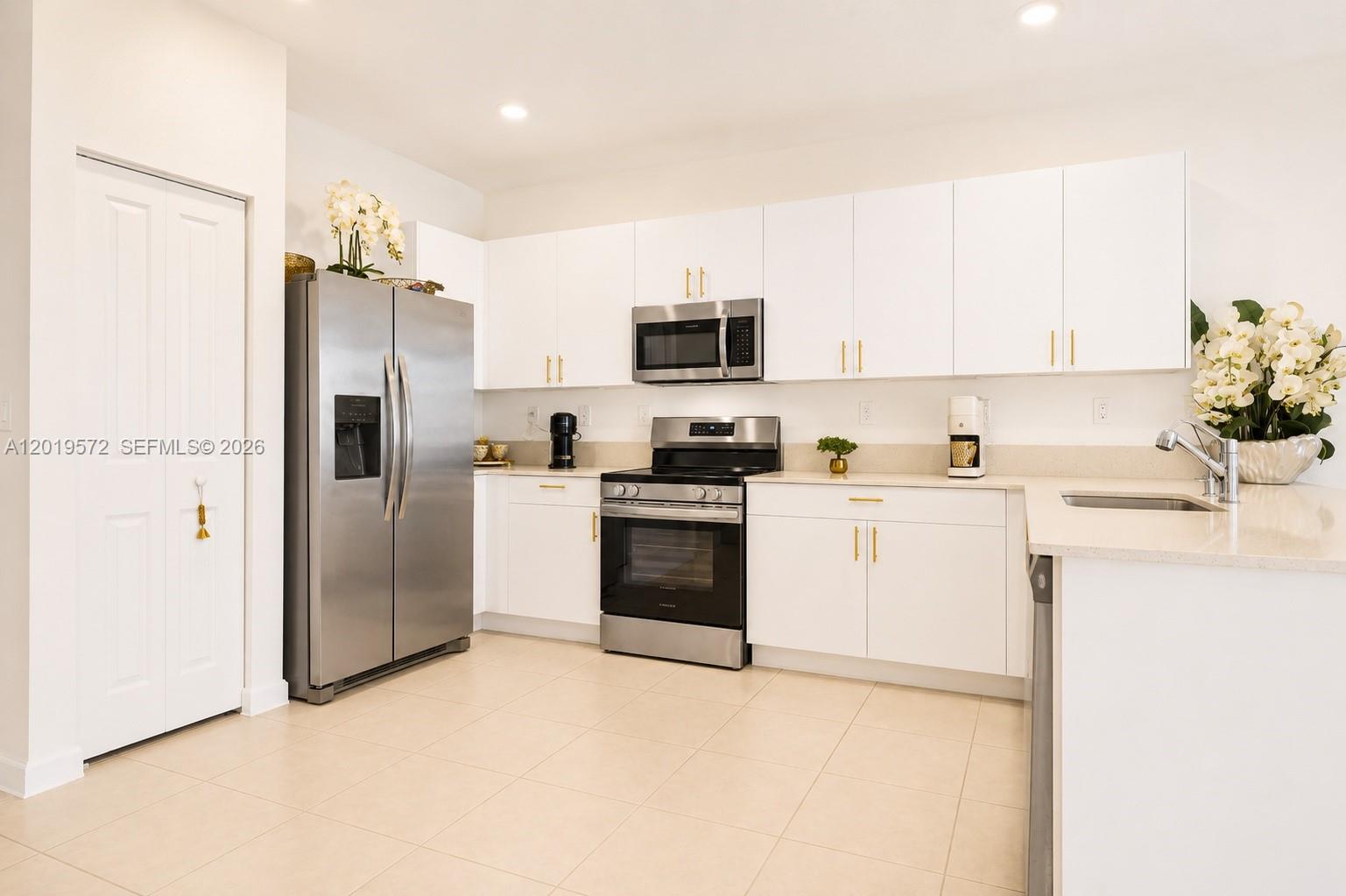 This kitchen features white cabinets, stainless steel appliances, and light-colored tile flooring — 12954 SW 231st St, Miami FL 33170, MIAMI, FL