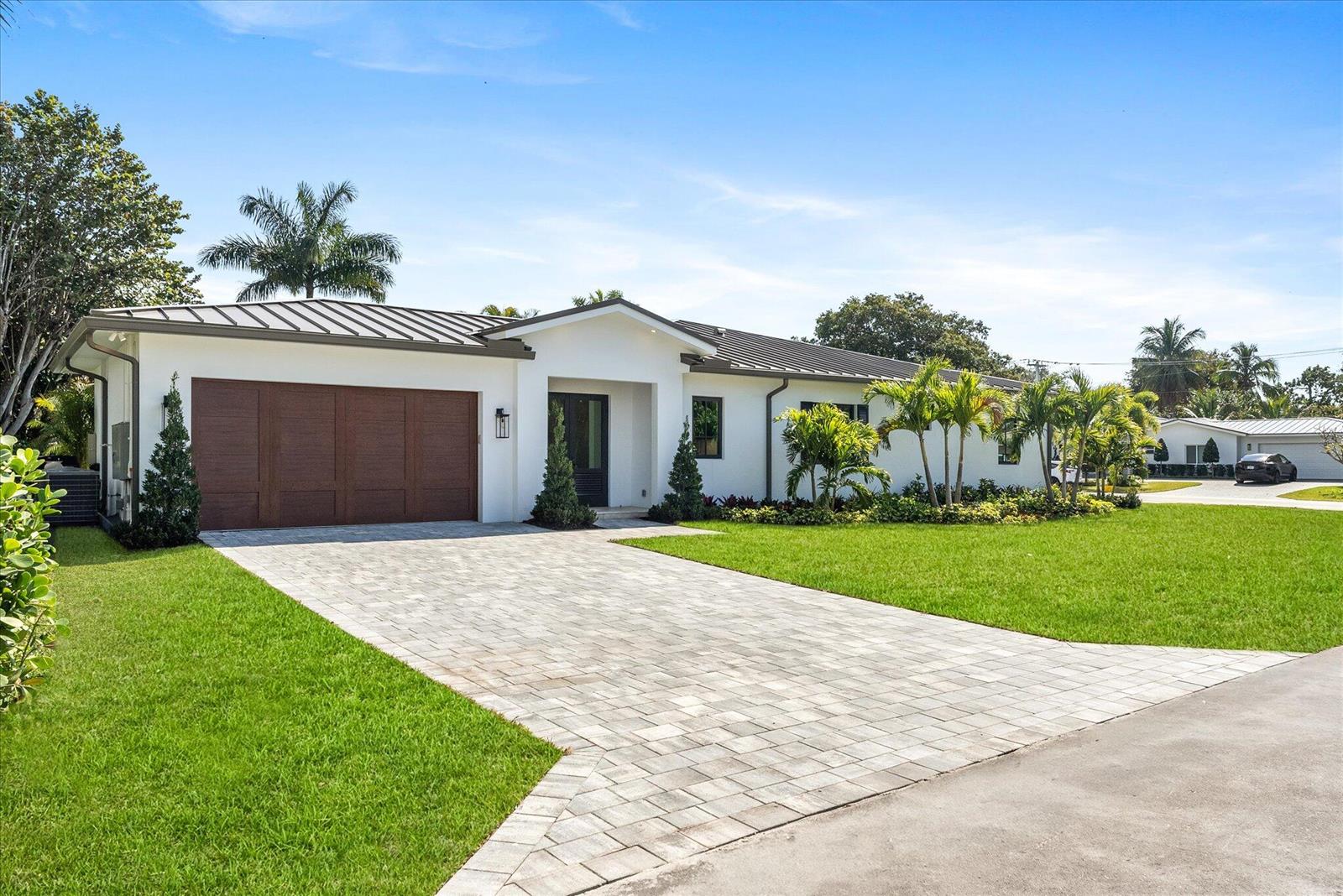 A single-story white house features a dark metal roof, a wood garage door, and landscaping — 715 Mission Hill Road, Boynton Beach FL 33435, BOYNTON BEACH, FL