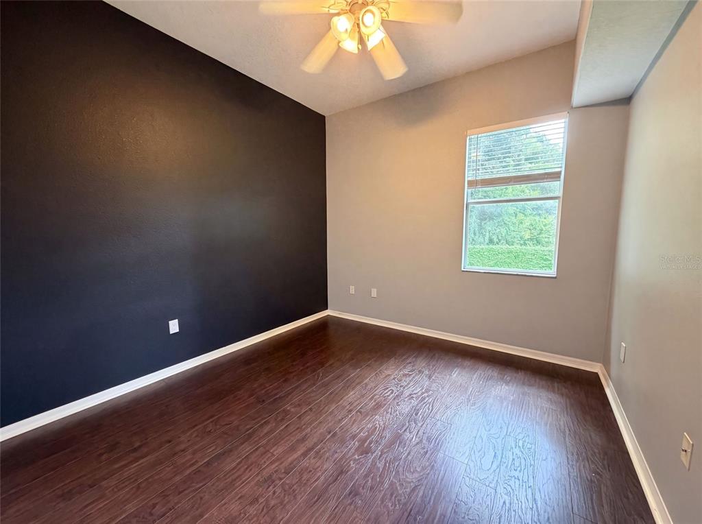 An empty room features dark wood flooring, a black accent wall, and a ceiling fan — 222 TAYLOR BAY LANE, BRANDON, FL