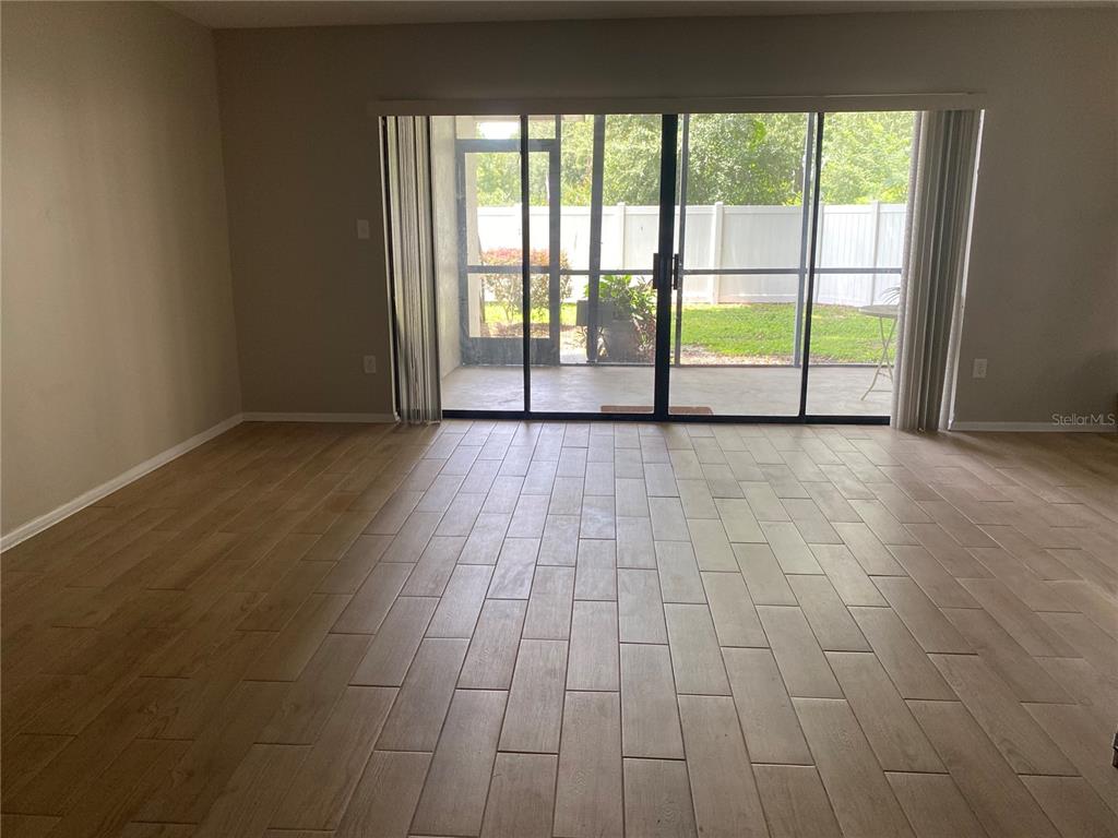 An empty room features light wood-look tile flooring and sliding glass doors leading to a patio — 4400 CASTLEPALM ROAD, ORLANDO, FL