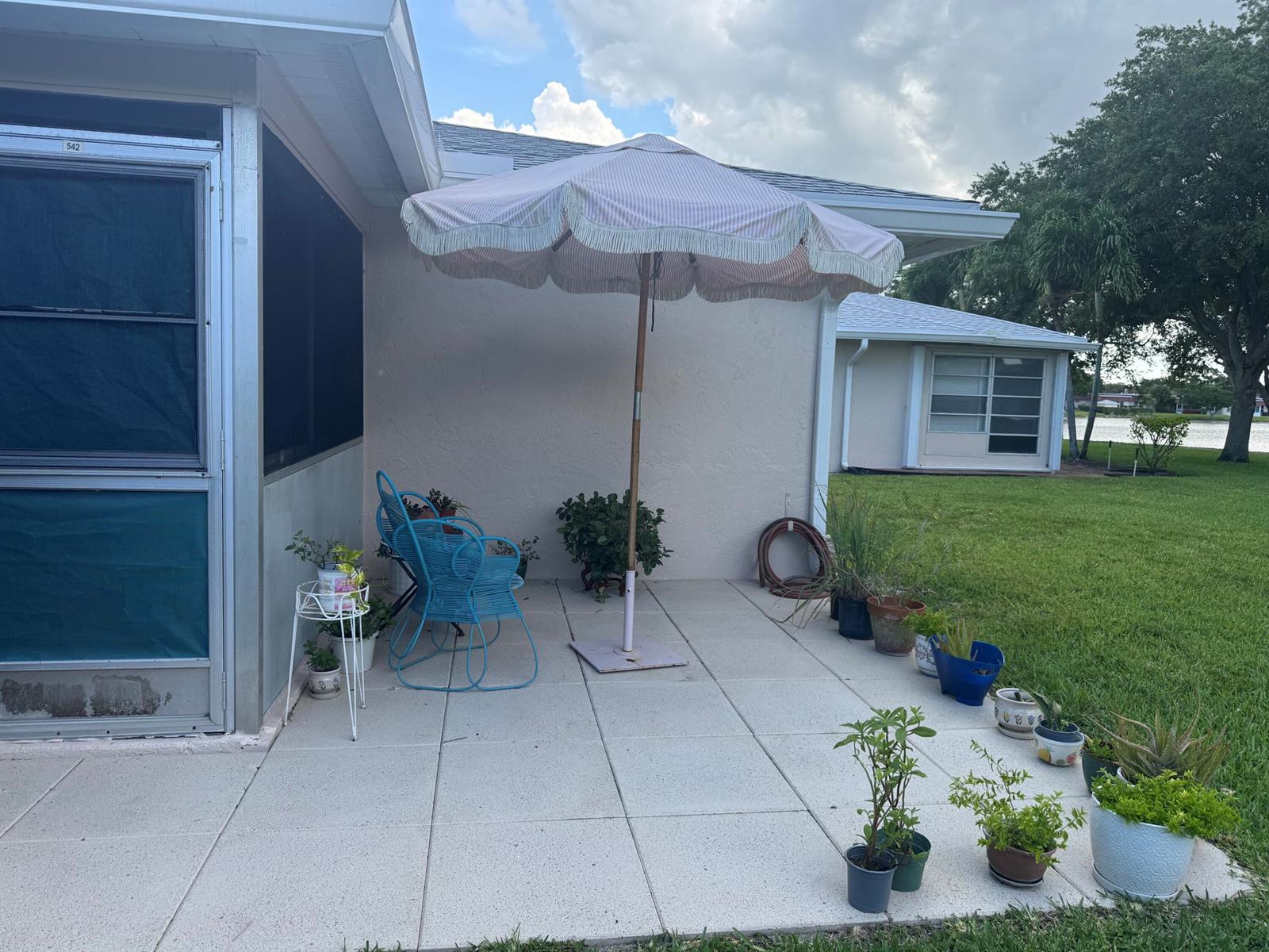 A paved patio features a striped umbrella, blue chairs, and various potted plants — 542 Franconia Circle, Lake Worth FL 33467, LAKE WORTH, FL