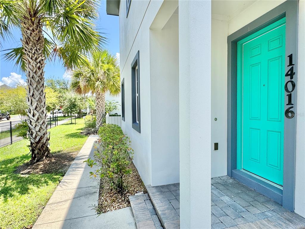 A bright turquoise front door with house numbers is set into a white exterior wall — 14016 DUNANT LANE, ORLANDO, FL