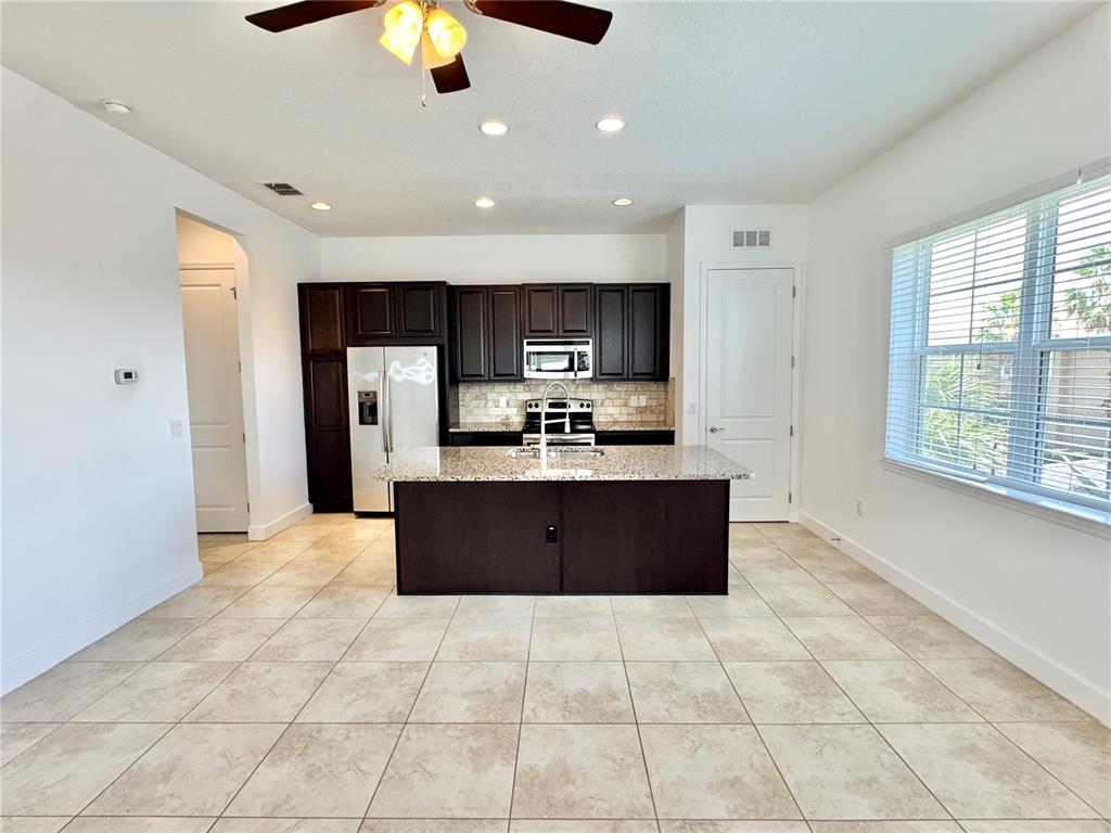 A kitchen features dark wood cabinets, granite countertops, a central island, and tile flooring — 14016 DUNANT LANE, ORLANDO, FL