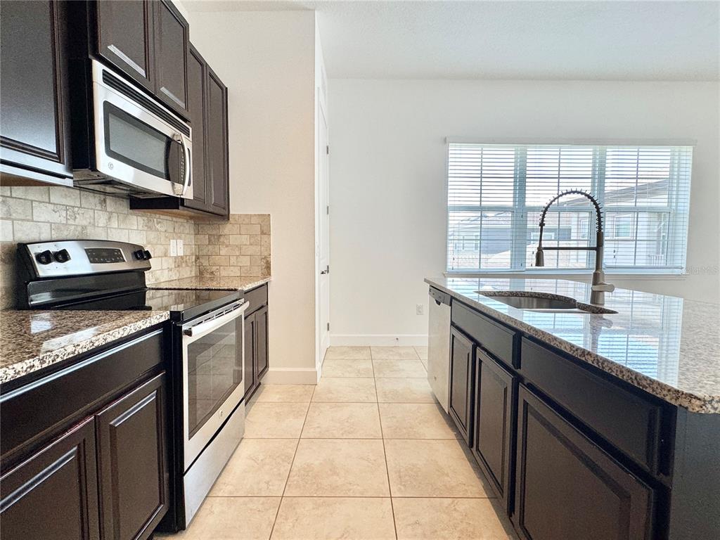 A kitchen features dark wood cabinets, granite countertops, stainless steel appliances, and a center island — 14016 DUNANT LANE, ORLANDO, FL