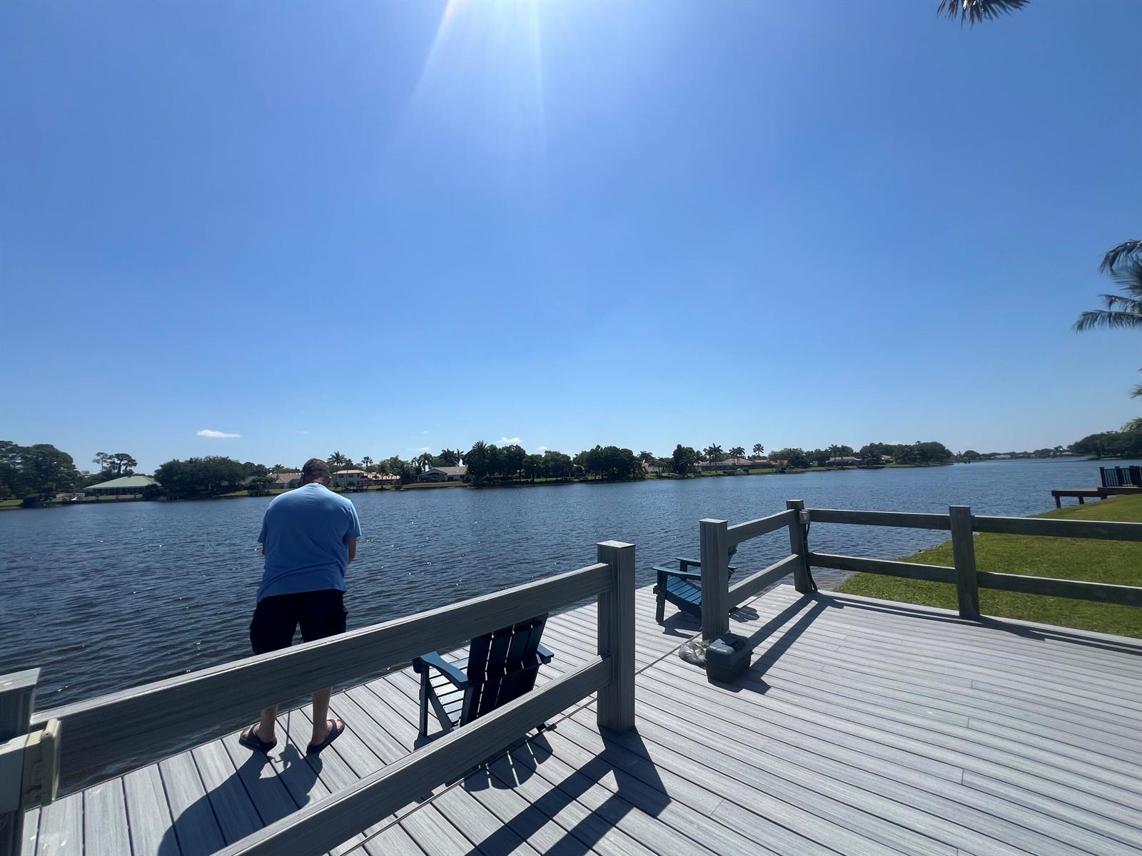 A man stands on a gray composite deck overlooking a lake with a wooden railing — 13646 Callington Drive, Wellington FL 33414, WELLINGTON, FL
