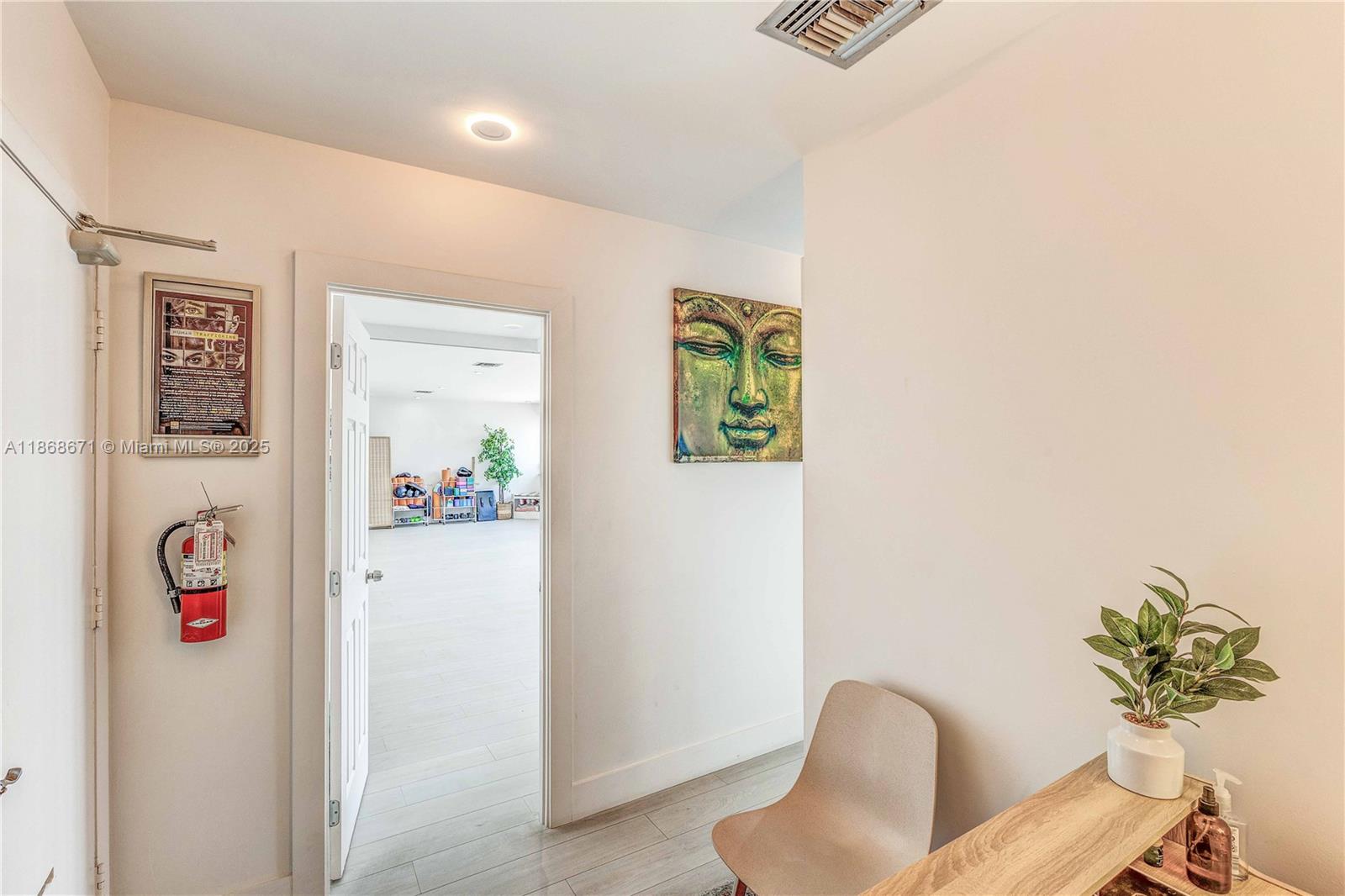 A hallway features a fire extinguisher, a Buddha painting, a chair, and a doorway to a room — 1385 SW 22nd St # 201, Miami FL 33145, MIAMI, FL