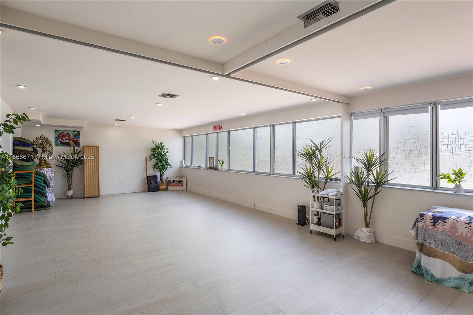 A spacious, minimalist yoga studio features light wood-look flooring, large windows, and recessed lighting — 1385 SW 22nd St # 201, Miami FL 33145, MIAMI, FL