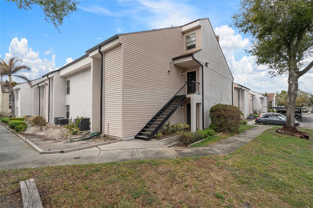 An exterior view of a two-story apartment building with beige siding and an outdoor staircase — 4821 PURITAN CIRCLE UNIT 104, TAMPA, FL