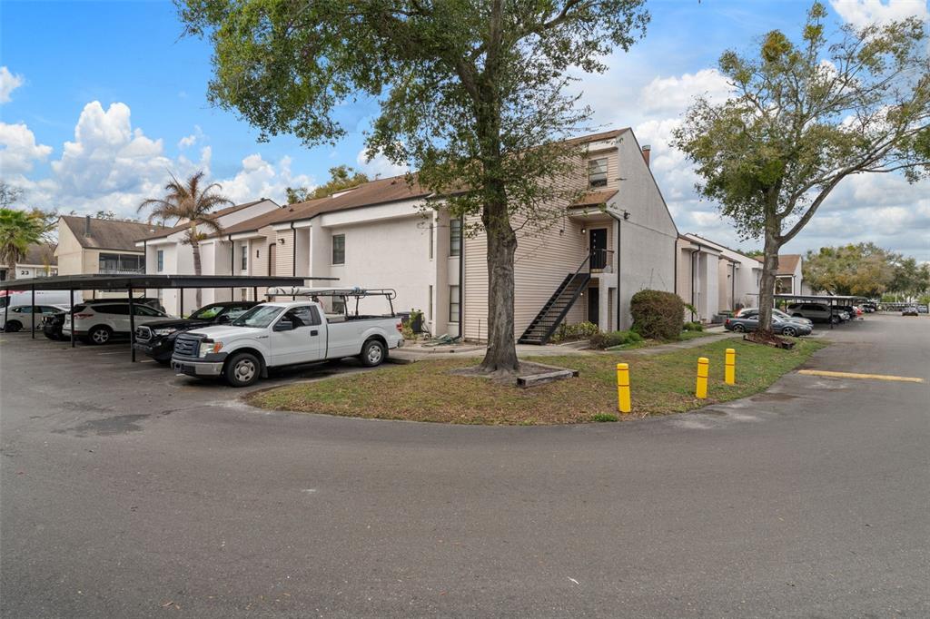 A multi-story apartment building with a parking lot and covered carports in the foreground — 4821 PURITAN CIRCLE UNIT 104, TAMPA, FL