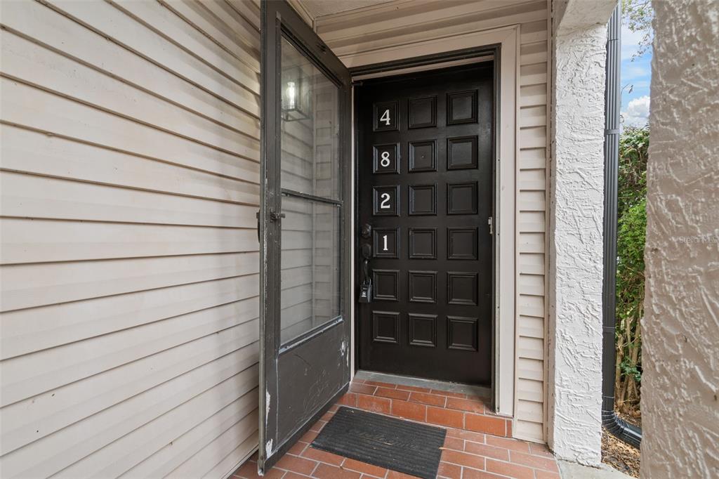 A black front door with the number 4821 is set within a brick-floored entryway — 4821 PURITAN CIRCLE UNIT 104, TAMPA, FL