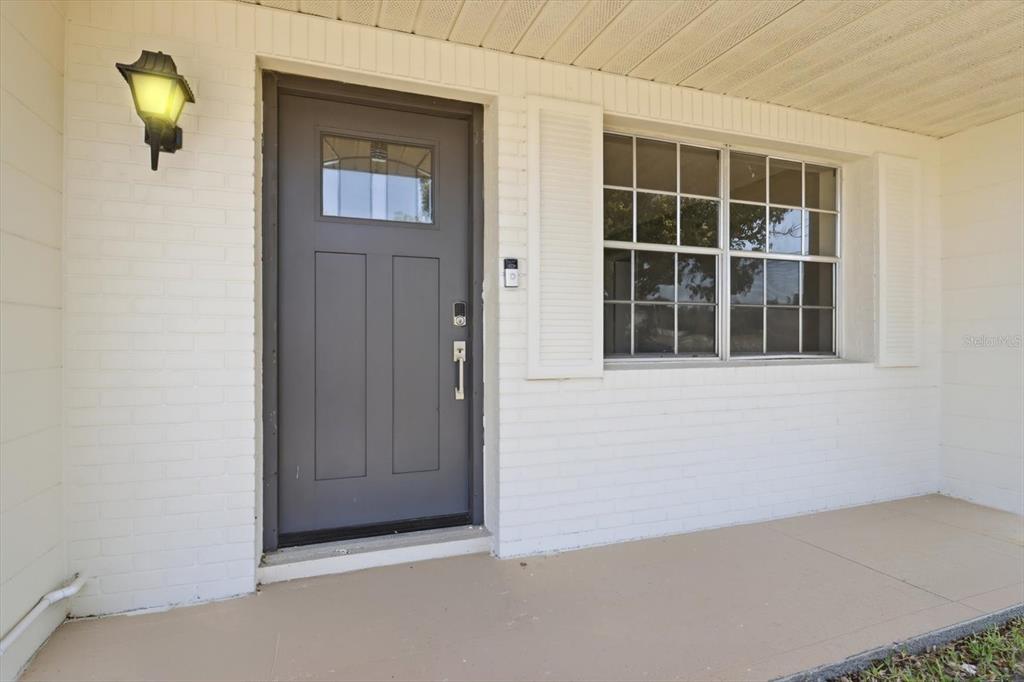 A gray front door with a window sits beside a window on a white brick wall — 5188 WOODRIDGE LANE, SPRING HILL, FL