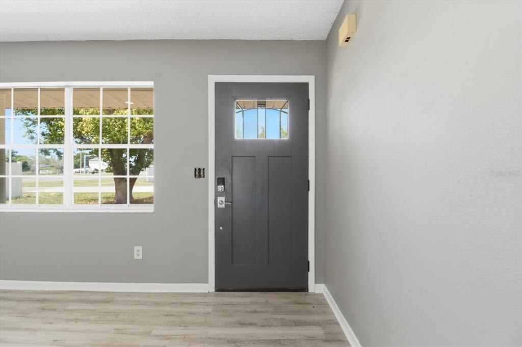 A room with gray walls, light wood-look flooring, a window, and a dark gray front door — 5188 WOODRIDGE LANE, SPRING HILL, FL