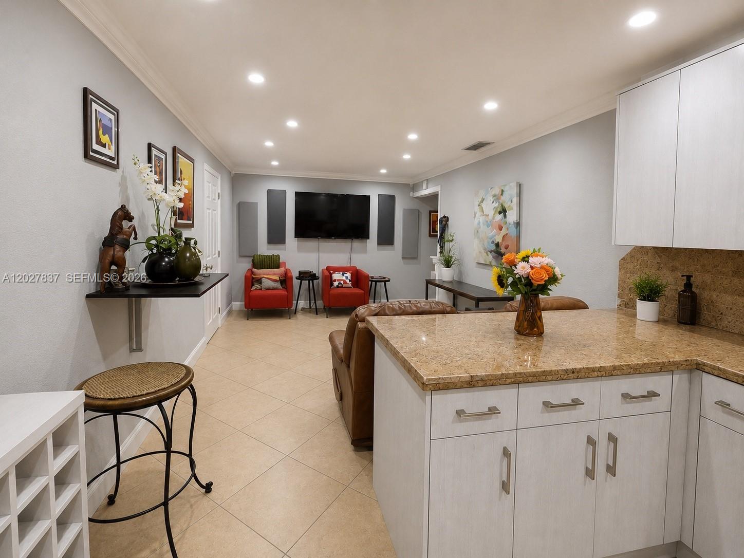 A kitchen island overlooks a living area with a television, red chairs, and tile flooring — 7513 Grant Ct # A, Hollywood FL 33024, HOLLYWOOD, FL