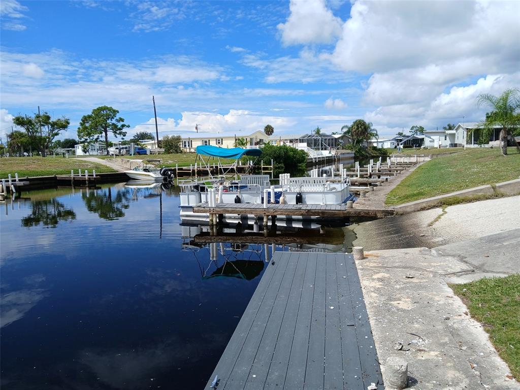 A boat dock with a pontoon boat sits on a canal near residential homes — 167 VIA MADONNA, ENGLEWOOD, FL