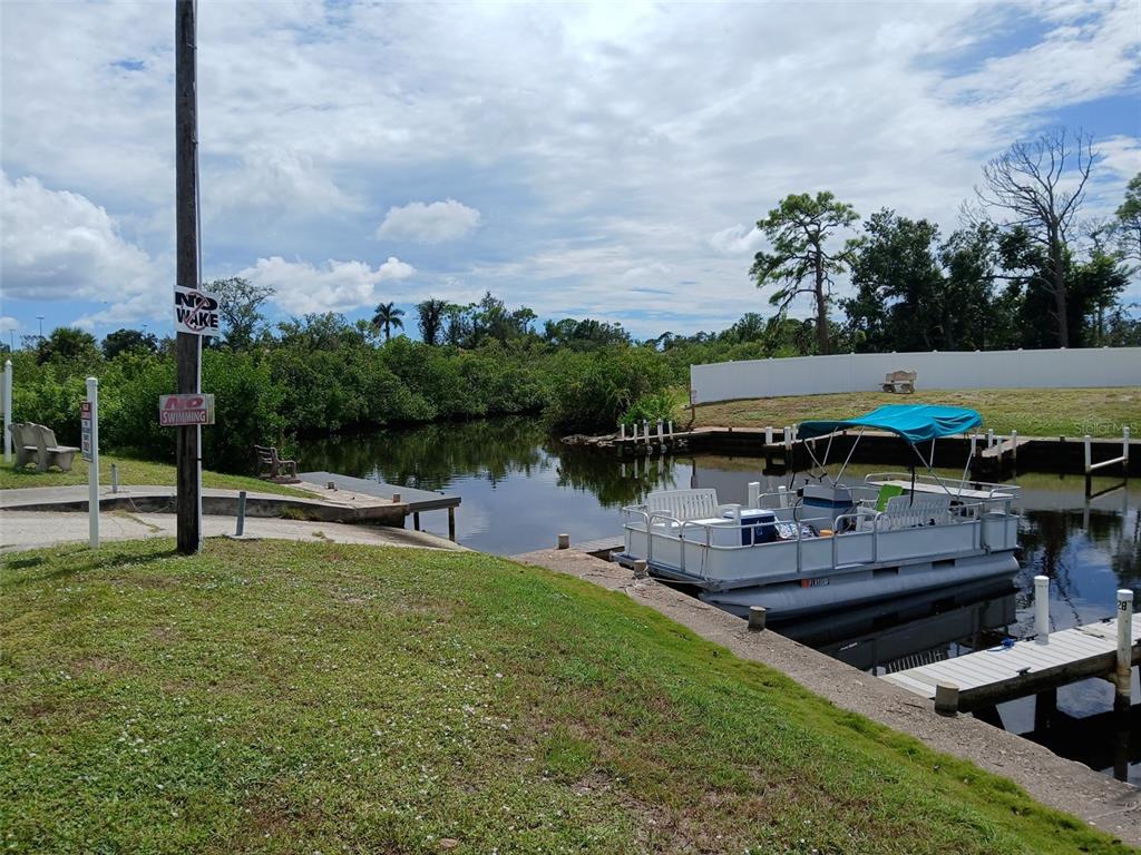 A pontoon boat is docked at a concrete bulkhead along a canal with mangroves — 167 VIA MADONNA, ENGLEWOOD, FL