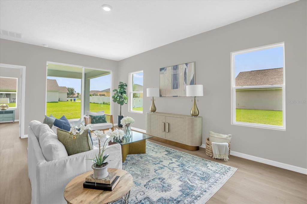 A bright living room features light wood flooring, a white sofa, and large windows — 5834 ESCALON DRIVE, SEBRING, FL